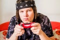 Young man with dreadlocks and serious face playing video games with a joystick sitting on an orange couch Royalty Free Stock Photo