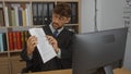 Young man dressed as a judge or lawyer in his office, analyzing documents in front of a computer, surrounded by books and files, Royalty Free Stock Photo