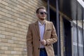 A young man dressed in a beige coat is walking down the street. A young bearded guy with a modern hairstyle and sunglasses Royalty Free Stock Photo