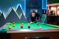 A young man dressed in black and smiling playing pool in a dark cocktail bar. Royalty Free Stock Photo