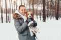 A young man in a snowy winter forest holds a dog breed Beagle. Royalty Free Stock Photo