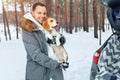 A young man dressed in a gray winter park in a snowy winter forest holds a dog named Beagle. Royalty Free Stock Photo