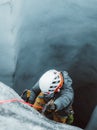 Young man dressed in a grey jacket using a rope to ascend the side of an icy cave. Royalty Free Stock Photo