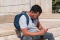 A young man dressed informally is sitting on a ladder, checking his phone