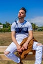 Young man dressed in white clothing and modern styling posing sitting on a wooden bench Royalty Free Stock Photo