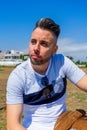 Young man dressed in white clothing and modern styling posing sitting on a wooden bench Royalty Free Stock Photo