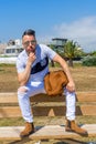 Young man dressed in white clothing and modern styling posing sitting on a wooden bench Royalty Free Stock Photo