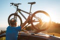 Young Man dresses modern cycling clothes and protective helmet installing his mountain bike on the car roof with sunset backlight Royalty Free Stock Photo
