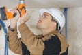 Young man drilling hole in white ceiling Royalty Free Stock Photo