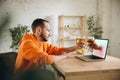 Young man drinking beer during meeting friends on virtual video call. Distance online meeting, chat together on laptop