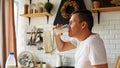 Young man drinking milk in kitchen. Adult male enjoying useful drink for breakfast Royalty Free Stock Photo