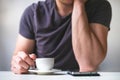 Young man drinking morning coffee and holding mobile phone. Coffee break. Man holding cup of fresh roasted coffee and looking at t