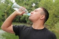 Young man drinks water on the background of beautiful green nature. quenches thirst. healthy lifestyle and health care Royalty Free Stock Photo