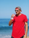 Young man drinks water from plastic bottle on ocean beach. Royalty Free Stock Photo