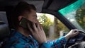 A young man is driving a car and talking on the phone in the daytime. Driver side view Royalty Free Stock Photo