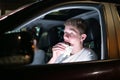 Young man eating burger in the car driving late at night in the parking lot