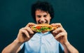 Young man eating a cheeseburger. Happy man in a fast-food restaurant eating a hamburger outdoors. Man with curly hair having Royalty Free Stock Photo