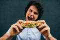 Young man eating a cheeseburger has pleasant expression. Hungry man in a fast food restaurant eating a hamburger outdoors. Man Royalty Free Stock Photo