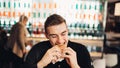 Young man eating fatty hamburger.Craving fast food.Enjoying guilty pleasure,eating junk food.Satisfied expression.Breaking diet Royalty Free Stock Photo