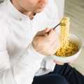 Young man is eating instant noodles from the white bowl. square