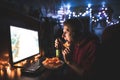 Young man eats chips, drinks beer and looks at the computer screen, sits at the table at home in a cozy room Royalty Free Stock Photo