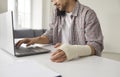 Young man with elastic bandage wrapped around his hand working on laptop computer Royalty Free Stock Photo