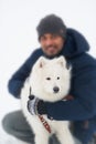 Young man embracing solid white fluffy dog in winter. Seective focus in dog.