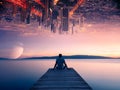 Young man enjoying the beautiful evening view of a lake from a wooden pier