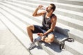 Young man exercising outside. Athlete sit on steps outside and thursting. Drinking water and enjoy it. Holding phone in Royalty Free Stock Photo