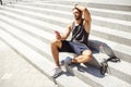 Young man exercising outside. Concentrated athlete sit on steps after training and relax. Holding phone in hand and Royalty Free Stock Photo