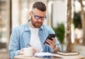 Young man in eyeglasses watching educational video on mobile phone, studying online at outdoor cafe Royalty Free Stock Photo