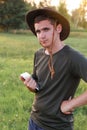 Young man farmer in cowboy hat at agricultural field on sunset holding tablet. Portrait of happy man standing on nature Royalty Free Stock Photo