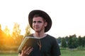 Young man farmer in cowboy hat at agricultural field on sunset with sun flare holding tablet. Portrait of happy man Royalty Free Stock Photo