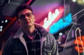 A young man fashionably dressed standing in the street at night. Illuminated signboards, neon, lights. Royalty Free Stock Photo