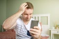 Young man feelling worried while holding phone or smartphone in his hand. One hand in his head Royalty Free Stock Photo