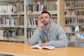 Young man with finger on his face thinking about possible answers with a book on the table in the library Royalty Free Stock Photo