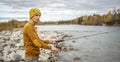 Man in a yellow sweater and hat is fishing on the river bank in the autumn forest with a spinning rod in his hands Royalty Free Stock Photo