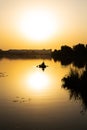 A young man is fishing on a lake from an inflatable small boat at a very beautiful orange sunset Royalty Free Stock Photo