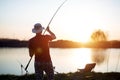 Young man fishing on lake at sunset enjoying hobby Royalty Free Stock Photo