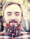 Young man with flowers in his beard natural blurred background close up