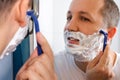 Young man with foam on his face shaves in front of a mirror. Royalty Free Stock Photo