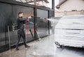 Young man foaming car by gun on car wash station outdoors.