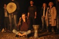 Young man, the follower of Ukrainian pagan cult, playing darbuka drum, people standing around, light from the burning fire set