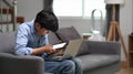 Young man freelancer working on laptop and using digital tablet and while sitting on couch at home. Royalty Free Stock Photo