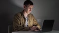 Young man freelancer works at night typing text on laptop Royalty Free Stock Photo