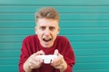 Young man with a gamepad in his hands plays videogames against the background of a turquoise wall