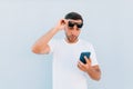 Young man gasping, shocked and appalled by a message he receives on blue background