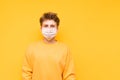 Young man in a gauze white mask isolated on a yellow background, looks into the camera with a serious face and poses for the