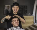 Young man getting haircut by happy barber while sitting in chair at barbershop