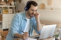 Young man getting remote education sitting by laptop in headphones